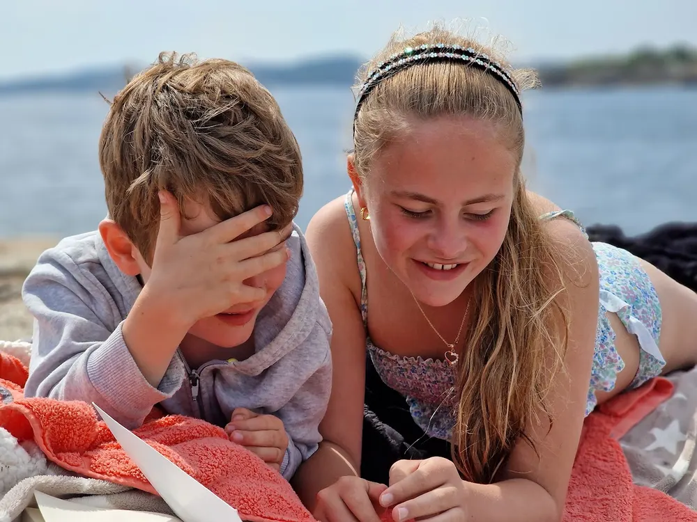 Ole og Nicoline ligger på et håndkle på svaberget en sommerdag, hode mot hode, og ler.